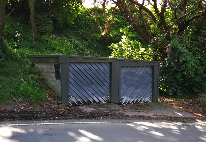 Two standalone car garages in a leafy setting.